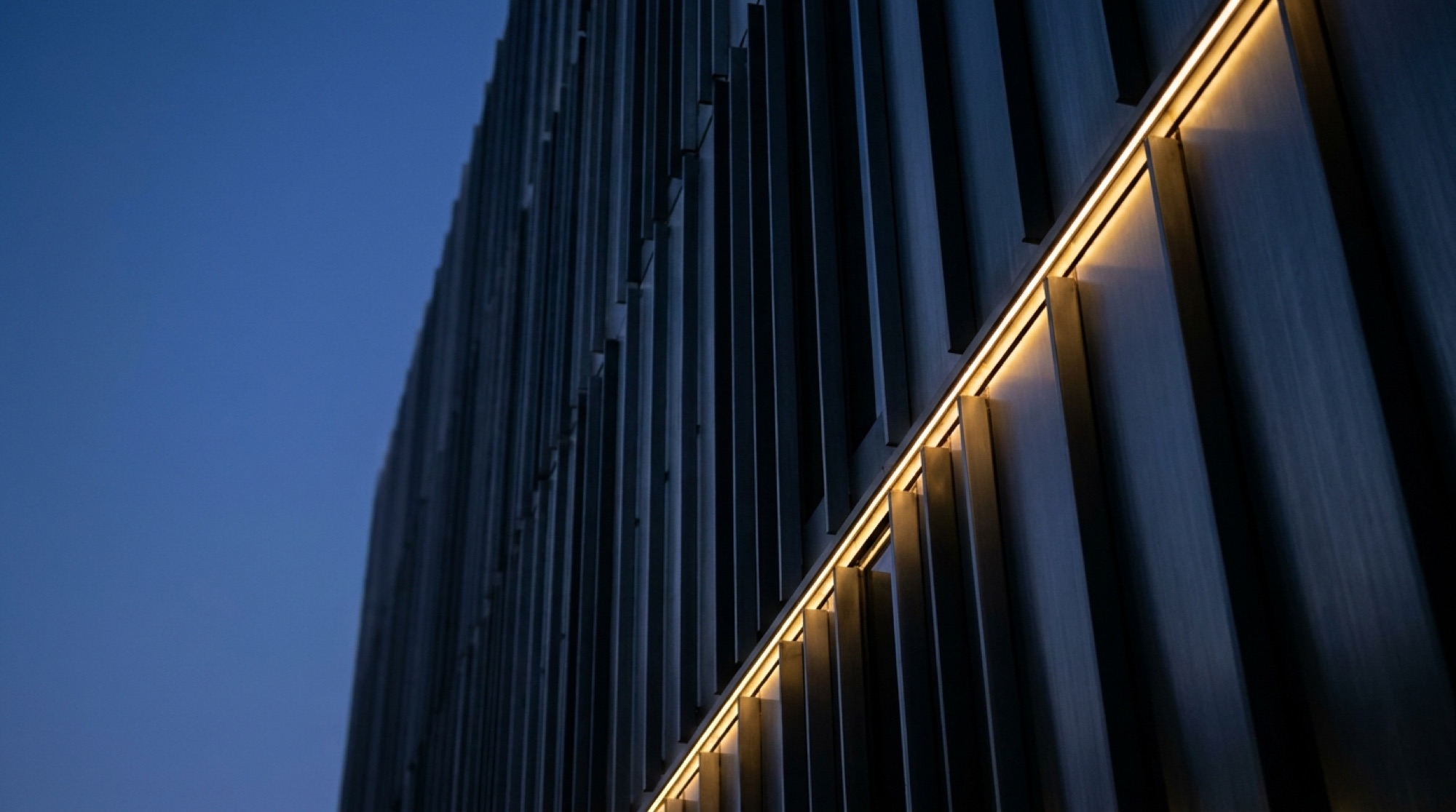 Steel building facade with a line of gold light at dusk